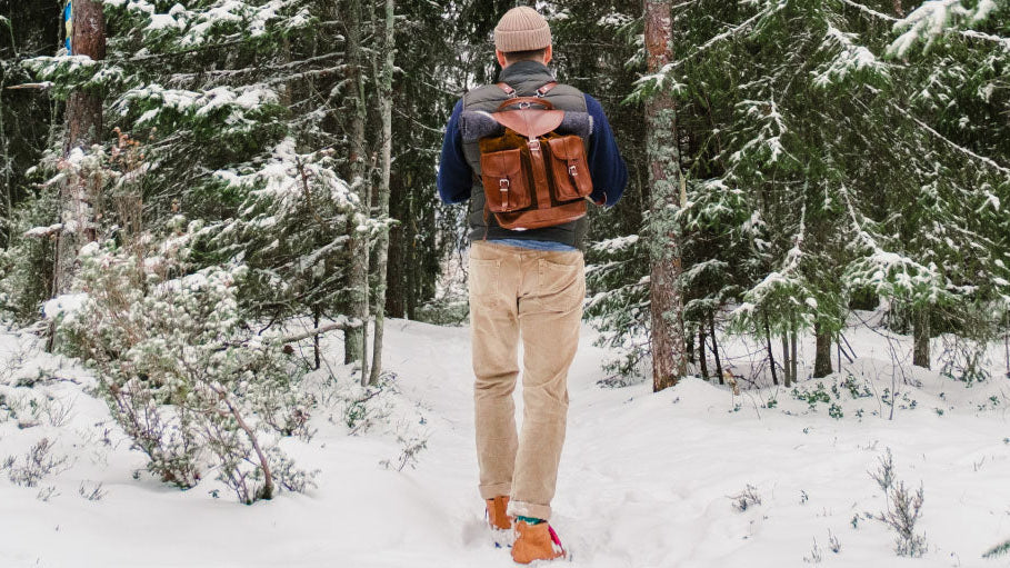 Eingeschneiter Wald in dem ein Mann einen Weg lang geht und einen Lederrucksack auf dem Rücken trägt