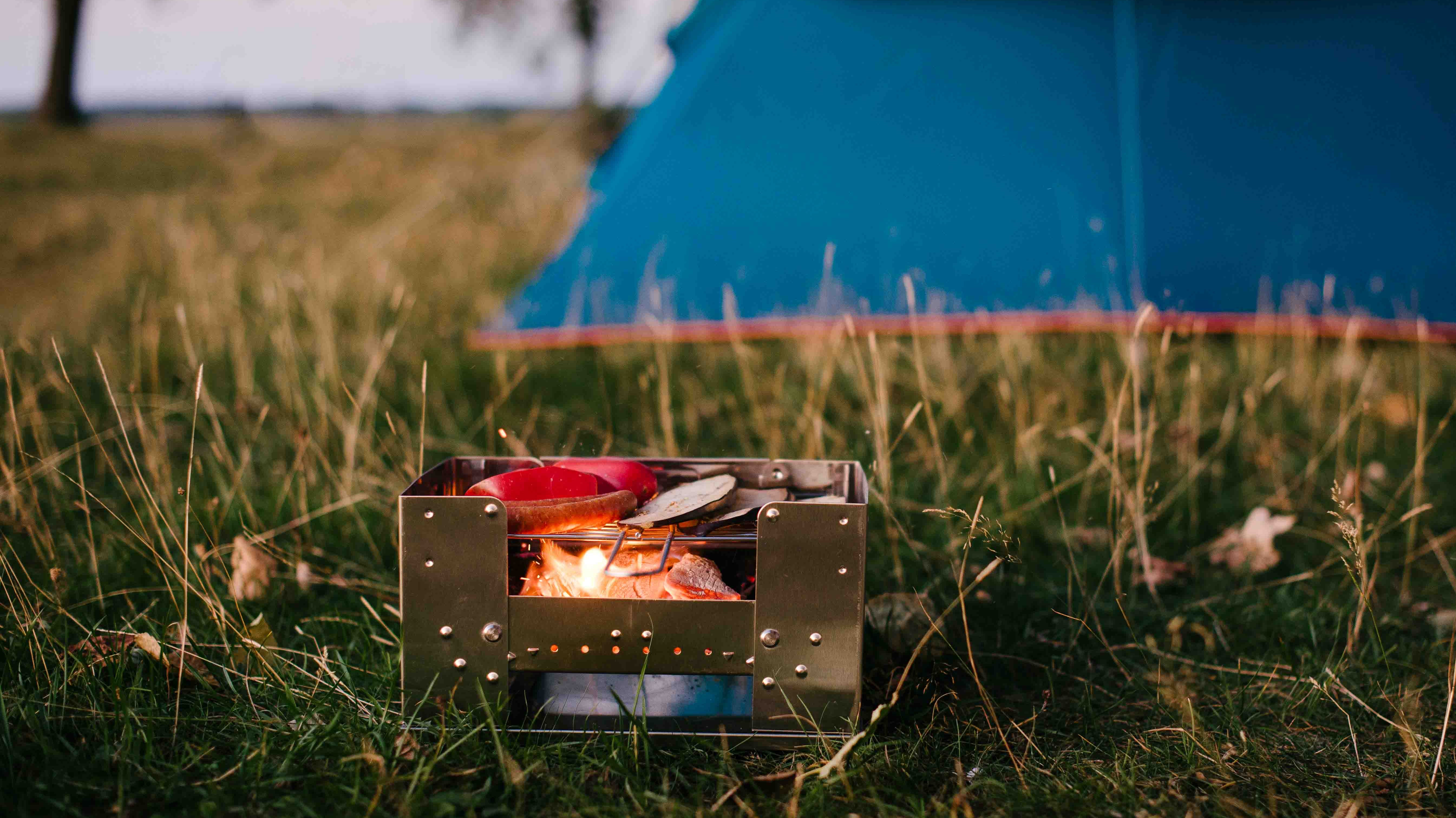 Esbit BBQ-Holzkohlegrill auf einer Wiese vor einem blauen Zelt