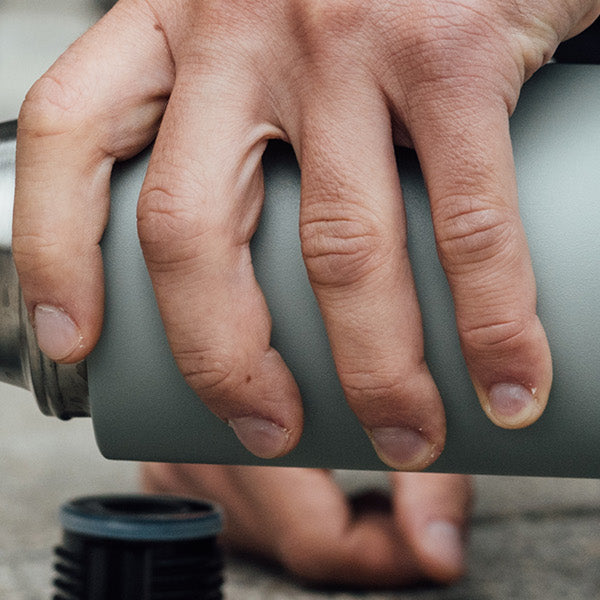 The SCULPTOR insulated flask in Stone Grey pours coffee into her mug.