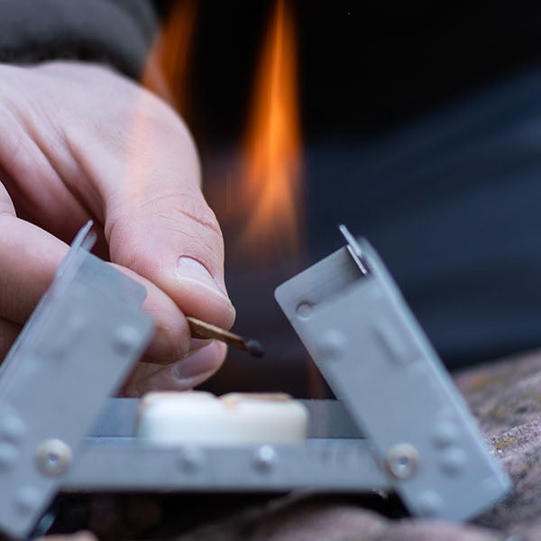 A man lights a 14 g dry fuel tablet in a small pocket stove.
