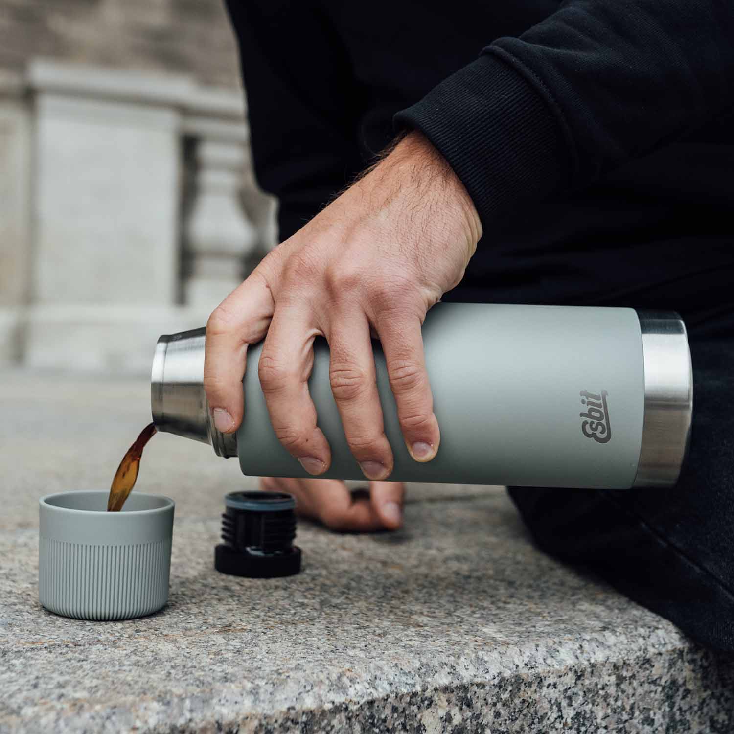 Mann schenkt Kaffee in den Trink-Becher der SCULPTOR Isolierflasche in Stone Grey.