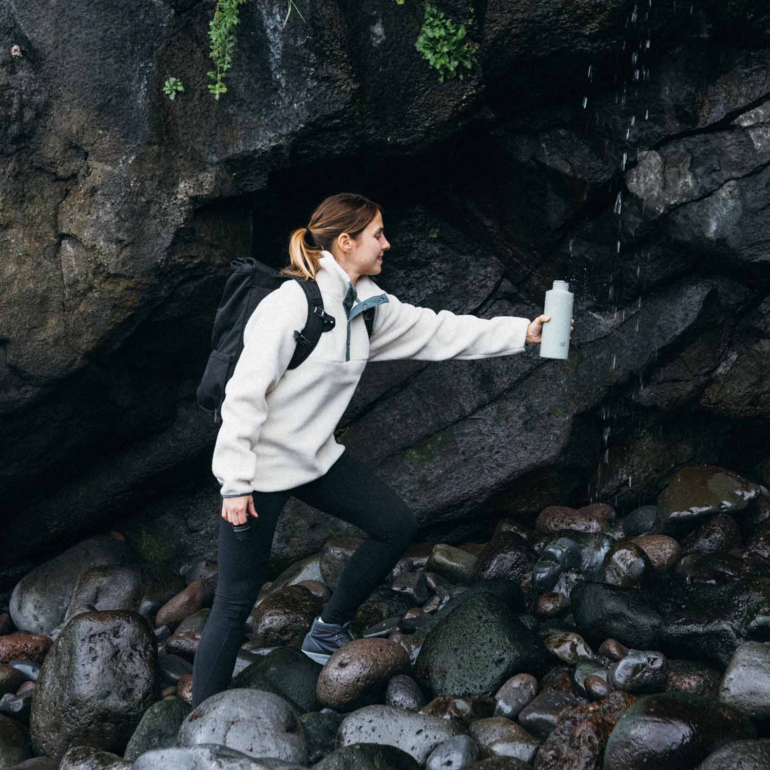 Frau füllt unterwegs ihre SCULPTOR Trinkflasche an einem Wasserfall auf.