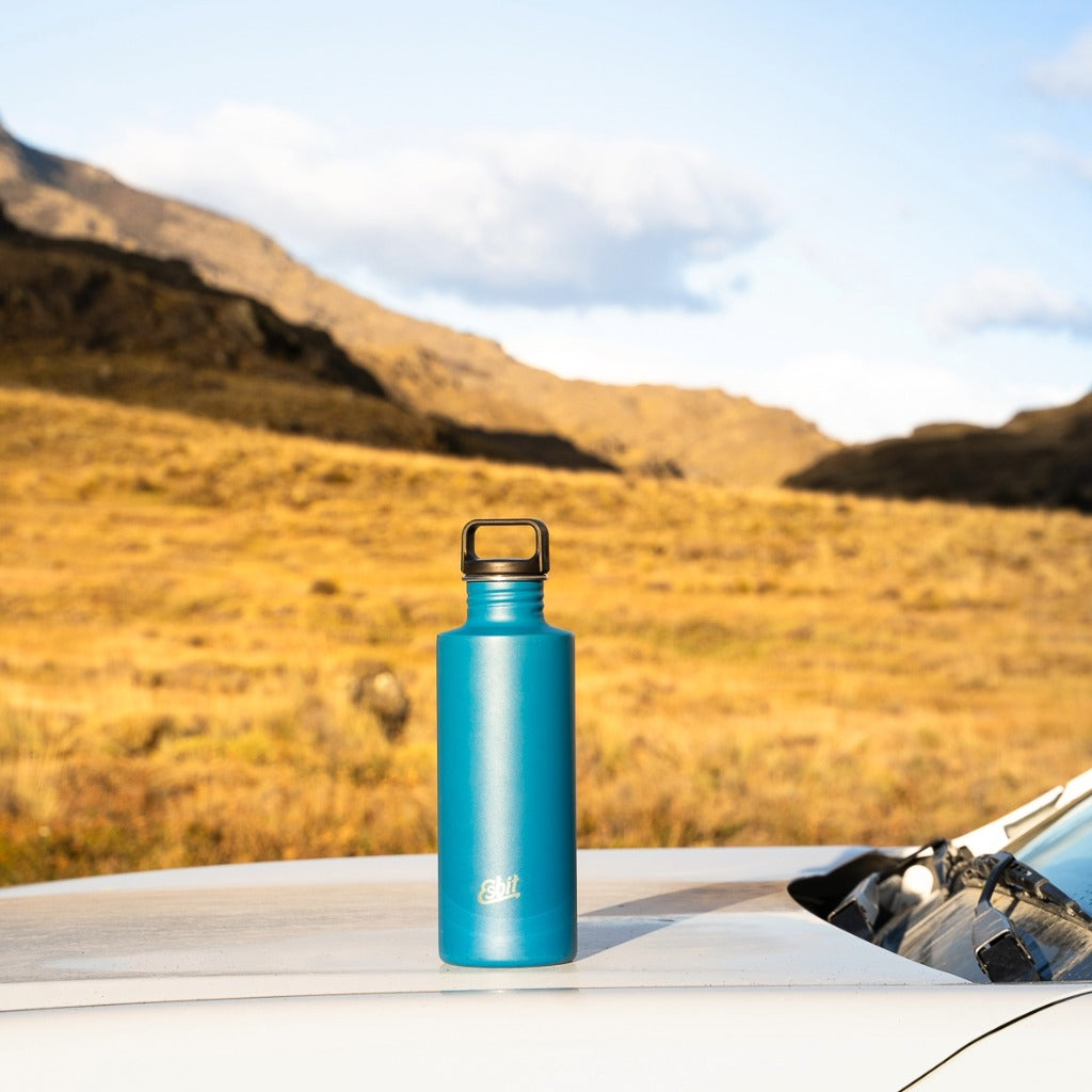 Esbit Edelstahl-Trinkflasche in Blau auf einem Fahrzeugdach vor einer weiten Berglandschaft.