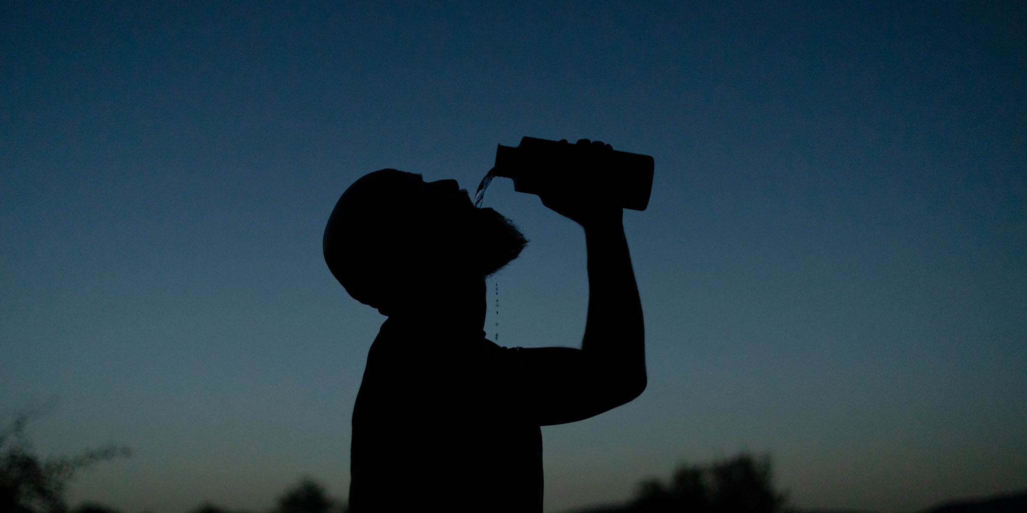Mann trinkt Wasser aus der SCULPTOR Trinkflasche in der Abenddämmerung.