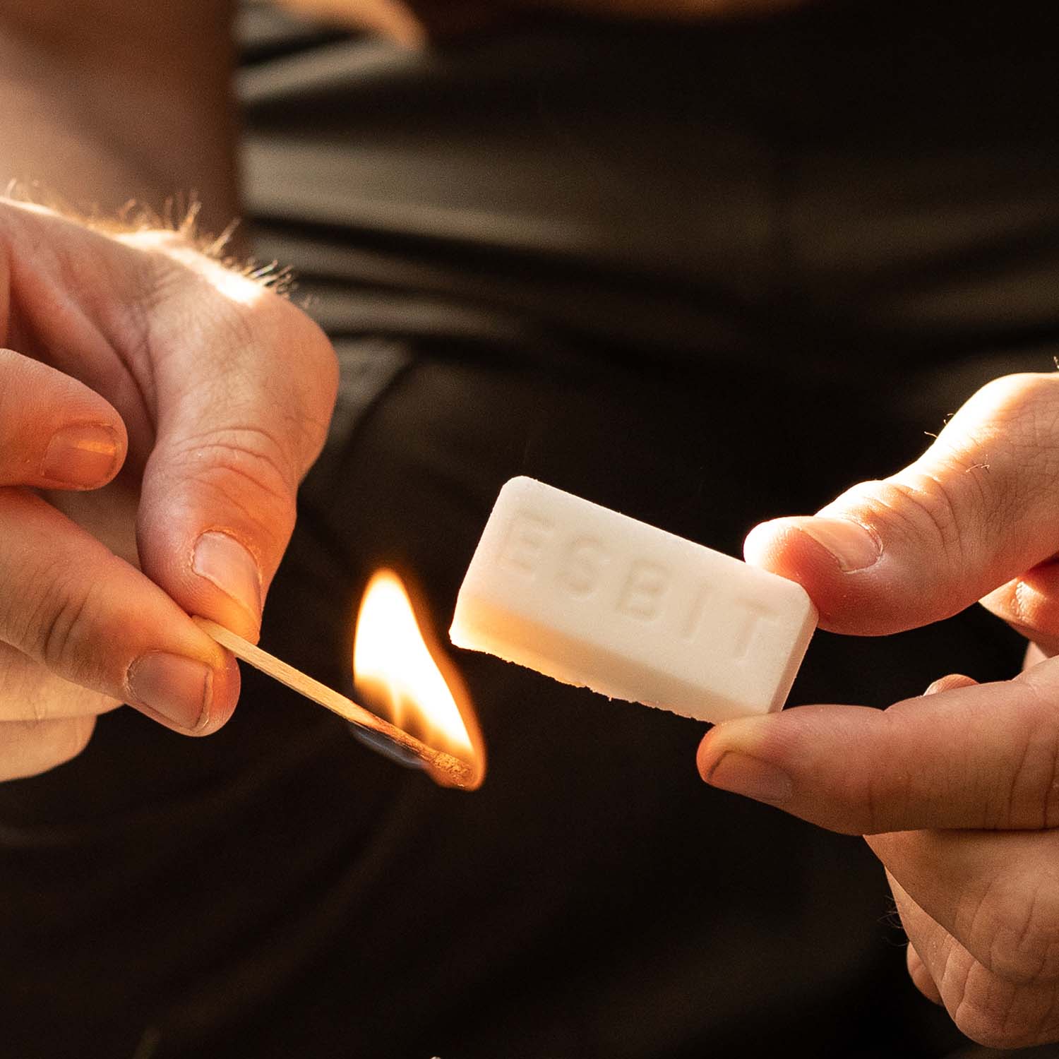 Mann zündet mit einem Streichholz eine halbe 27 Gramm Trockenbrennstoff-Tablette an.