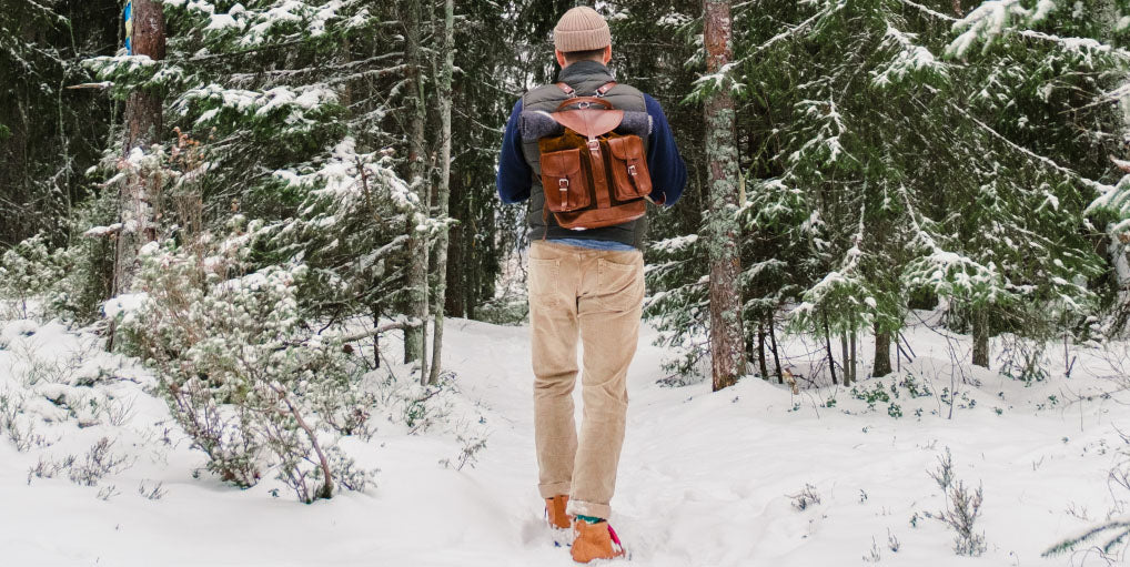 Eingeschneiter Wald in dem ein Mann einen Weg lang geht und einen Lederrucksack auf dem Rücken trägt