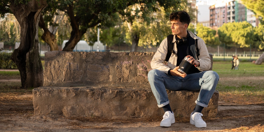 Junger Mann sitzt auf einem Stein im Park und hält Esbit Thermobehälter in der Hand