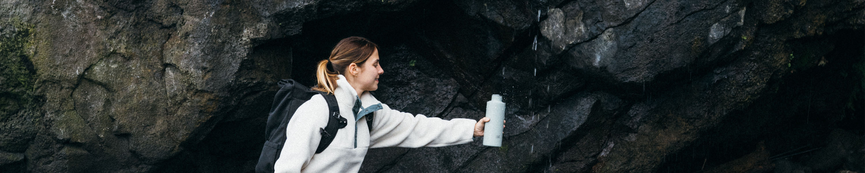 Frau füllt unterwegs ihre SCULPTOR Trinkflasche an einem Wasserfall auf