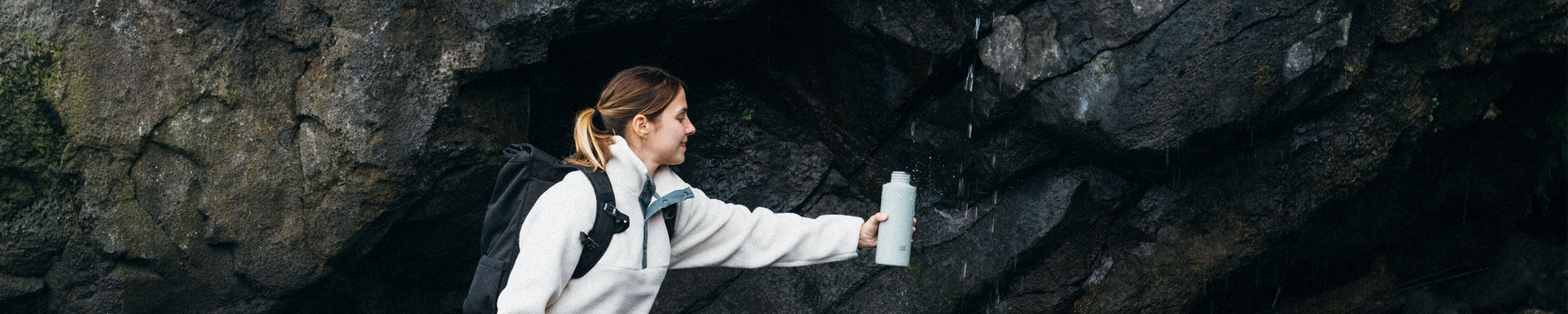 Frau füllt unterwegs ihre SCULPTOR Trinkflasche an einem Wasserfall auf