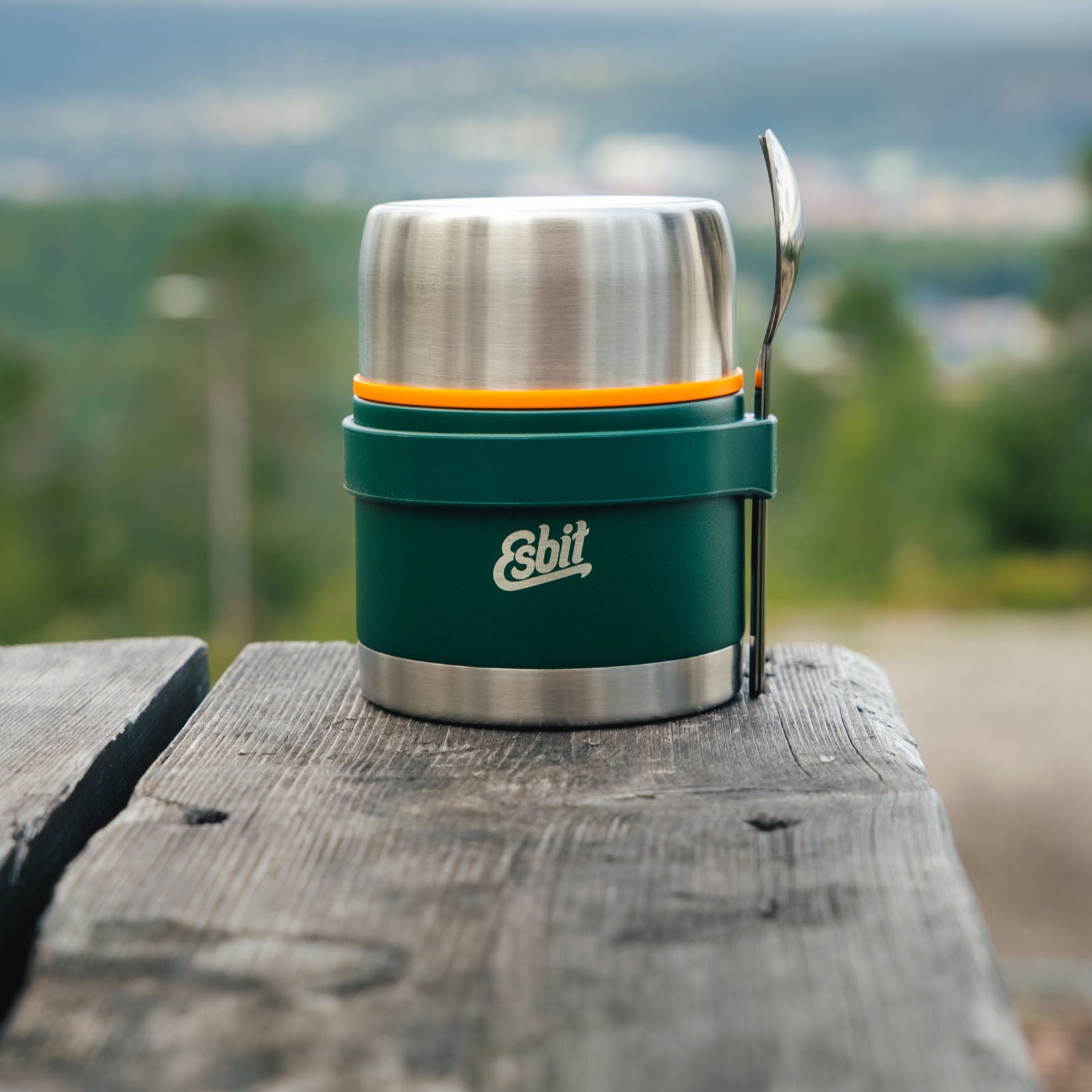 Grüner Esbit Food Jug mit Silikonband und Besteckset steht auf einem Holztisch in der Natur 