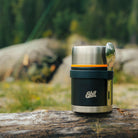 Schwarzer Esbit Food Jug mit Silikonband und Besteckset auf einem Baumstamm in der Natur 