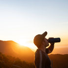 Person trinkt aus einer Esbit Edelstahl-Trinkflasche bei Sonnenuntergang in den Bergen.