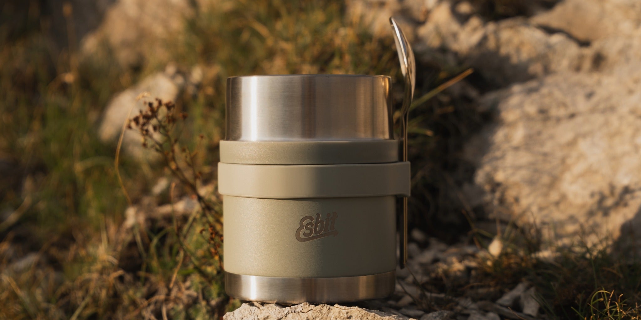 Esbit stainless steel thermos flask in Stone Grey with a colour-coordinated silicone strap and stainless steel cutlery in an outdoor setting.
