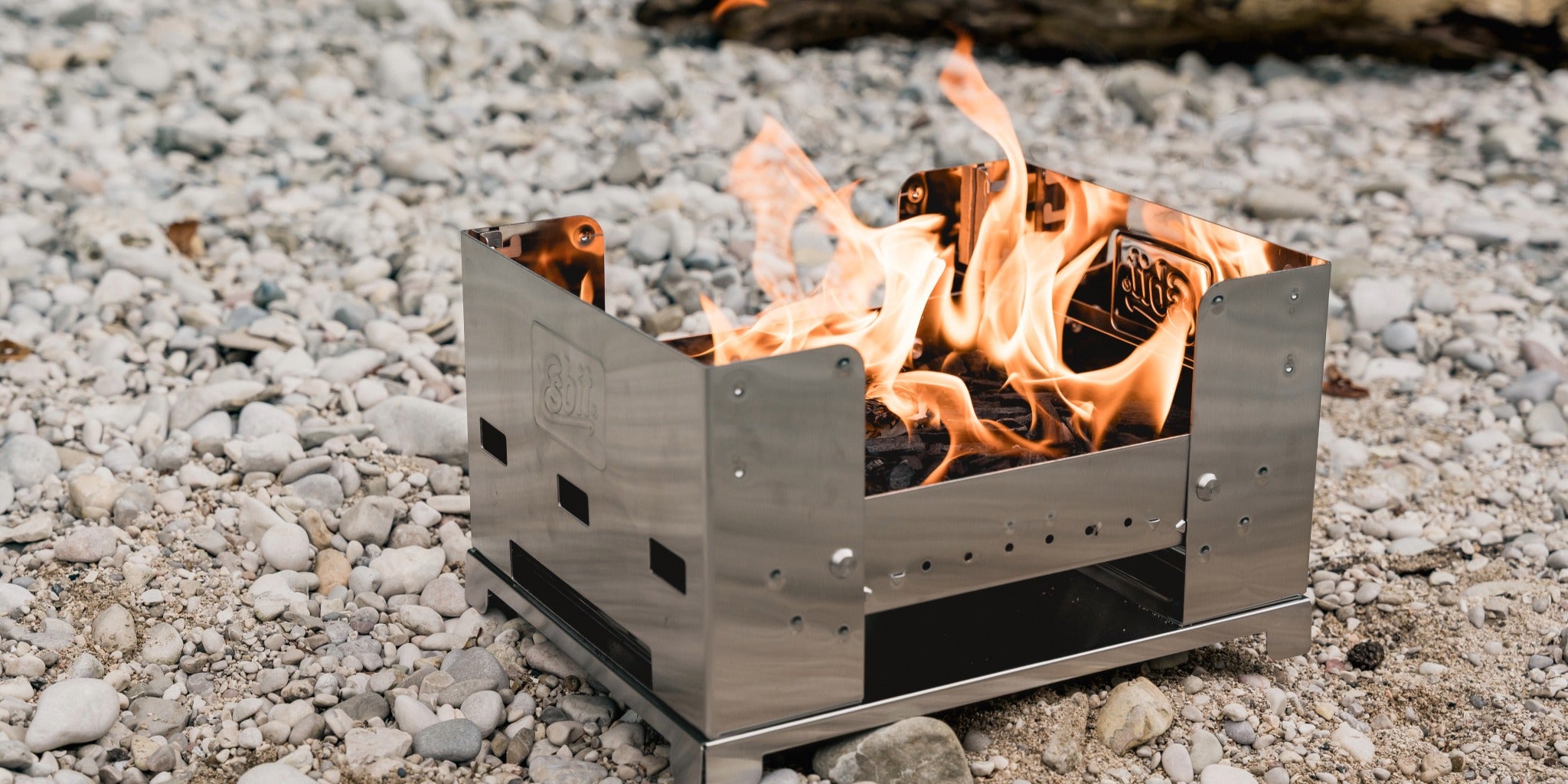 Esbit Edelstahlgrill mit brennendem Feuer auf steinigem Untergrund im Freien.