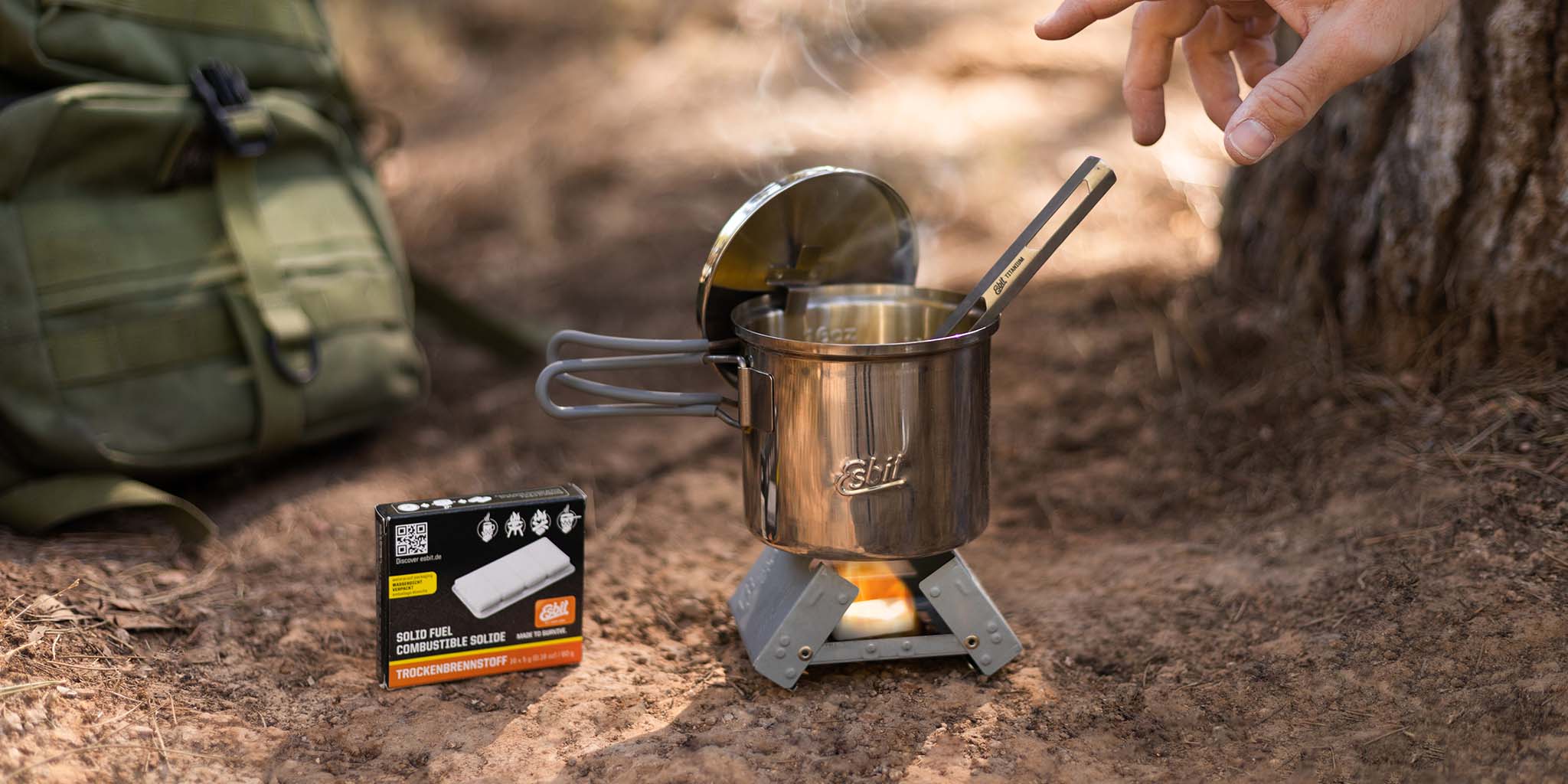 Edelstahl Camping Topf steht auf dem kleinen Taschenkocher, in dem eine Trockenbrennstoff-Tablette brennt